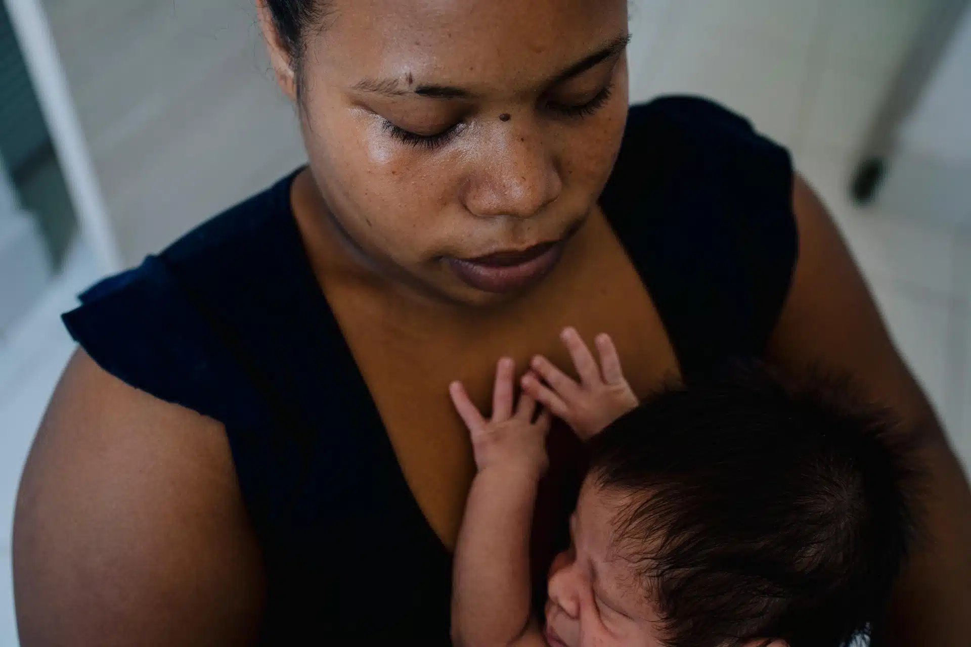 A mother cradles her sleeping newborn against her chest, the baby's tiny hand resting on her skin, in a quiet, tender moment
